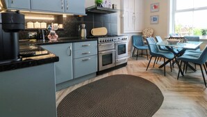 Een moderne keuken met grijze kastjes, een zwart aanrecht en een eethoek met blauwe stoelen en een glazen tafel.