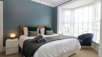 A bedroom with a bed, bedside tables, a chair, a window with blinds, and a chandelier.