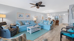 A living room with a sofa, armchair, coffee table, and ceiling fan. - Caper Beach Club 313 (Fort Myers Beach)