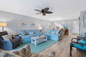 A living room with a sofa, armchair, coffee table, and ceiling fan. - Caper Beach Club 313 (Fort Myers Beach)