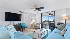 A living room with a television, two sofas, a coffee table, a ceiling fan, and a view to the outside. - Caper Beach Club 313 (Fort Myers Beach)