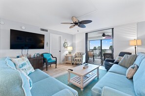 A living room with a television, two sofas, a coffee table, a ceiling fan, and a view to the outside. - Caper Beach Club 313 (Fort Myers Beach)