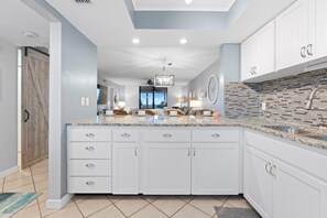 A modern kitchen with white cabinetry, a granite countertop, and a backsplash with black and gray tiles. - Caper Beach Club 313 (Fort Myers Beach)