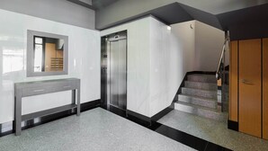 Un interior modern amb una paret de marbre, un mirall, una taula de consola gris, una escala i un ascensor.