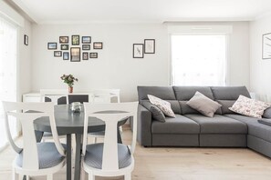 A living room with a grey sofa, white chairs, a dining table, and framed pictures on the wall. - Ardantza Bidea - baskeyrentals (Zumaia)