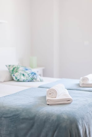 A neatly made bed with a folded towel, a pillow with a leaf pattern, and a green candle on a bedside table. - Ardantza Bidea - baskeyrentals (Zumaia)