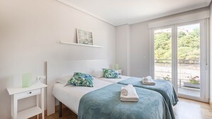 Habitació d'hotel amb dos llits, un escriptori petit, una estant amb una imatge i un balcó amb vistes.