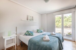 A hotel room with two beds, a small desk, a shelf with a picture, and a balcony with a view. - Ardantza Bidea - baskeyrentals (Zumaia)
