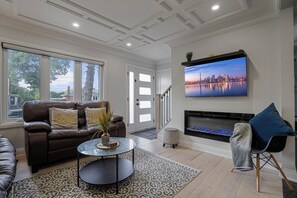A living room with a sofa, a coffee table, a fireplace, and a TV on the wall. - Luxury Toronto Stay with BBQ, Gazebo, Games & Parking (Toronto)