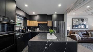 A modern kitchen with a central island, built-in appliances, and a dining area with a brown leather sofa.