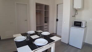 Un coin repas avec une table dressée pour quatre personnes, un four à micro-ondes et un placard contenant des vêtements suspendus.