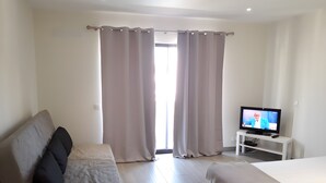 Une chambre d’hôtel avec un lit, un canapé, une télévision et une fenêtre avec des rideaux.
