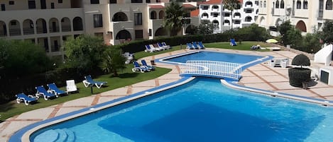 A swimming pool with a blue border, surrounded by lounge chairs and a paved deck.