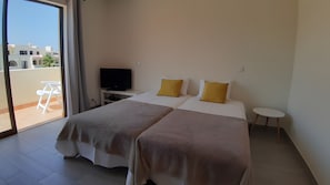 Ein Hotelzimmer mit zwei Betten, einem Fernseher, einem kleinen Tisch und Blick ins Freie.