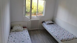 Pieni huone, jossa on kaksi erillistä sänkyä, patteri ja ikkuna, josta avautuu näkymä vehreään maisemaan.