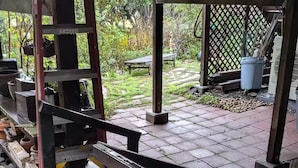 Ett takförsett utomhusområde med en metallkonstruktion, en grön soptunna och en träbänk.
