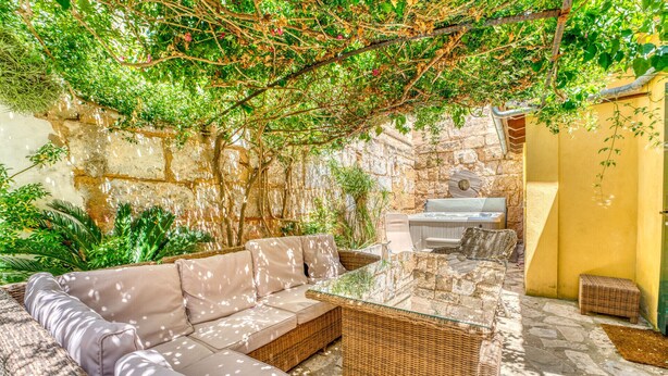 A covered outdoor seating area with a stone wall, a grill, and lush greenery. - House with Jacuzzi Can Grande Alcudia (Alcudia)