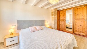 A bedroom with a bed, bedside lamps, a wooden wardrobe, and a stone wall. - House with Jacuzzi Can Grande Alcudia (Alcudia)