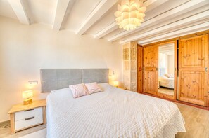 A bedroom with a bed, bedside lamps, a wooden wardrobe, and a stone wall. - House with Jacuzzi Can Gran Alcudia (Alcudia)