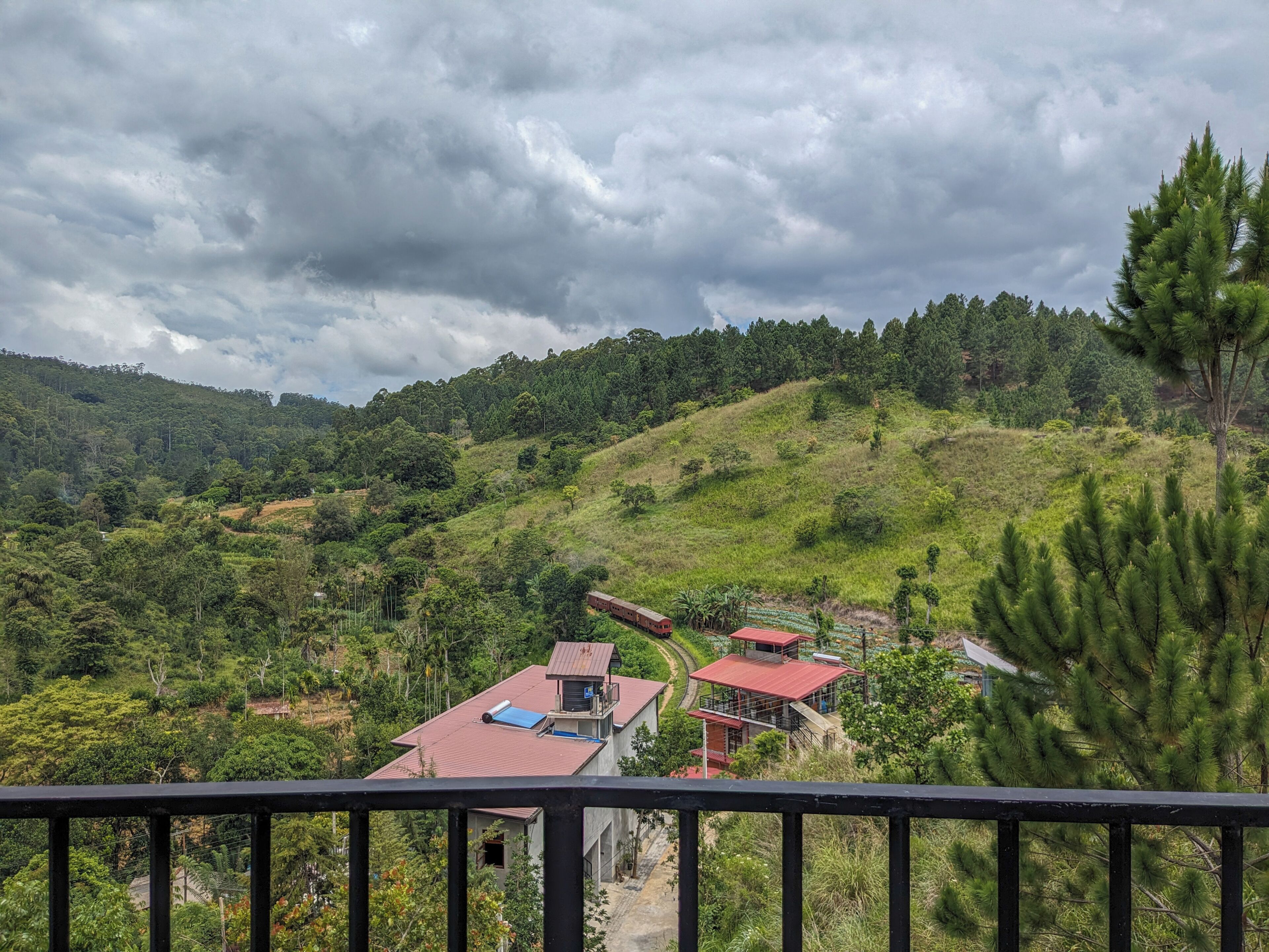 A rural landscape with a house and a small building with a red roof, surrounded by greenery and hills.