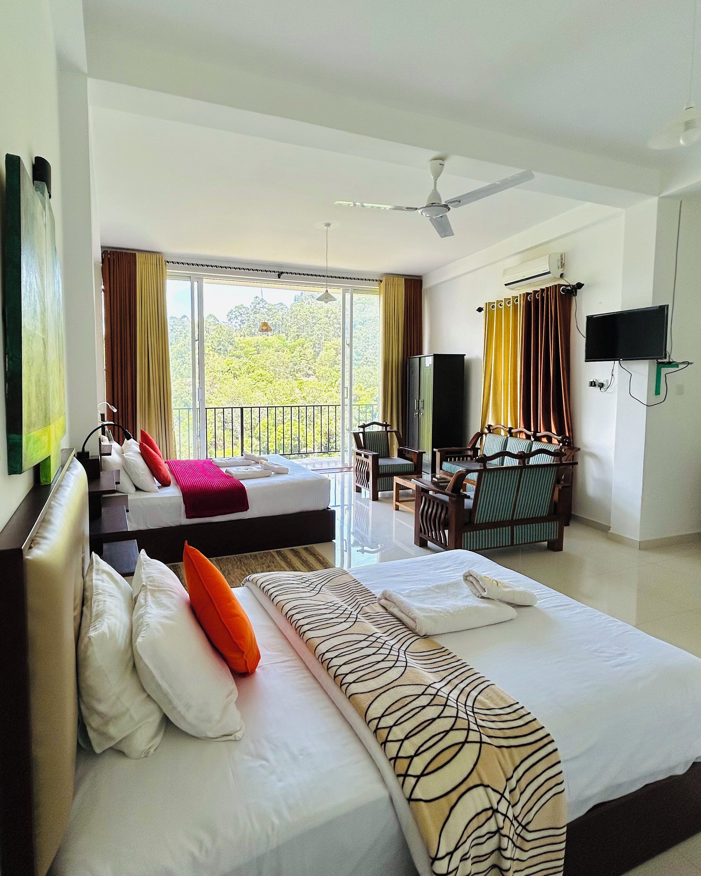 A hotel room with a large bed, a smaller bed, a desk with a chair, a television, and a balcony with curtains.