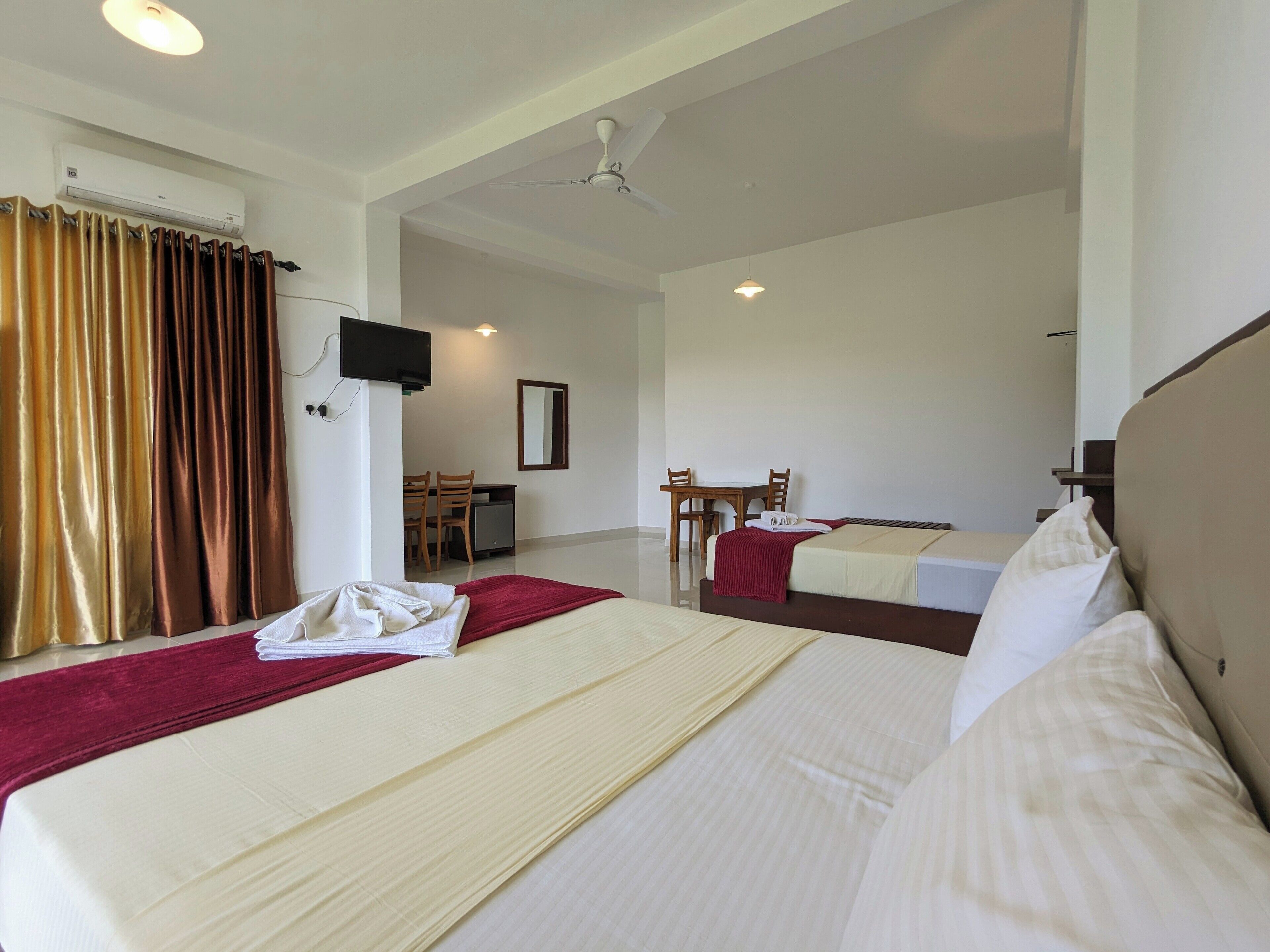 Ein Hotelzimmer mit zwei Betten, einem Schreibtisch, einem Stuhl, einem Fernseher und einem Deckenventilator.
