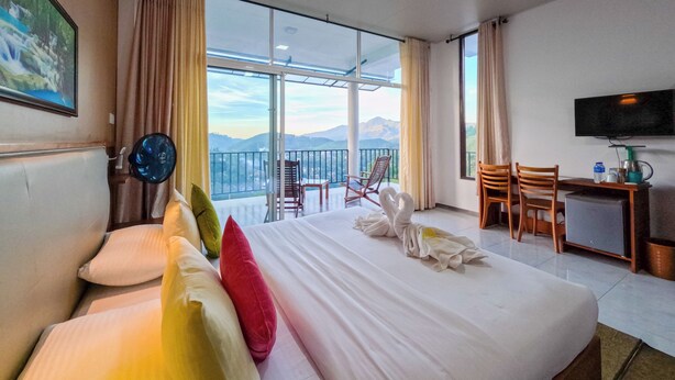 A hotel room with a large bed, a desk, a chair, a television, and a balcony with a mountain view.