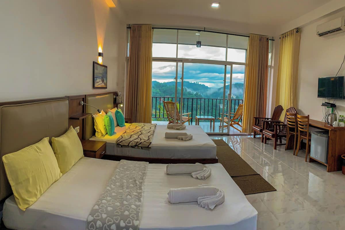 Habitación de hotel con dos camas, un balcón con sillas, televisión y vistas a las montañas.