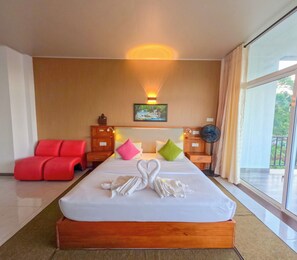 Una habitación de hotel con una cama grande, una silla roja, una mesita de noche, un cuadro en la pared y un ventanal amplio.