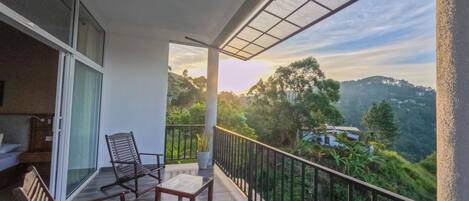 Un balcon offrant une vue sur un paysage montagneux, un coin salon avec des chaises et une table, et une porte vitrée donnant accès à un espace intérieur.