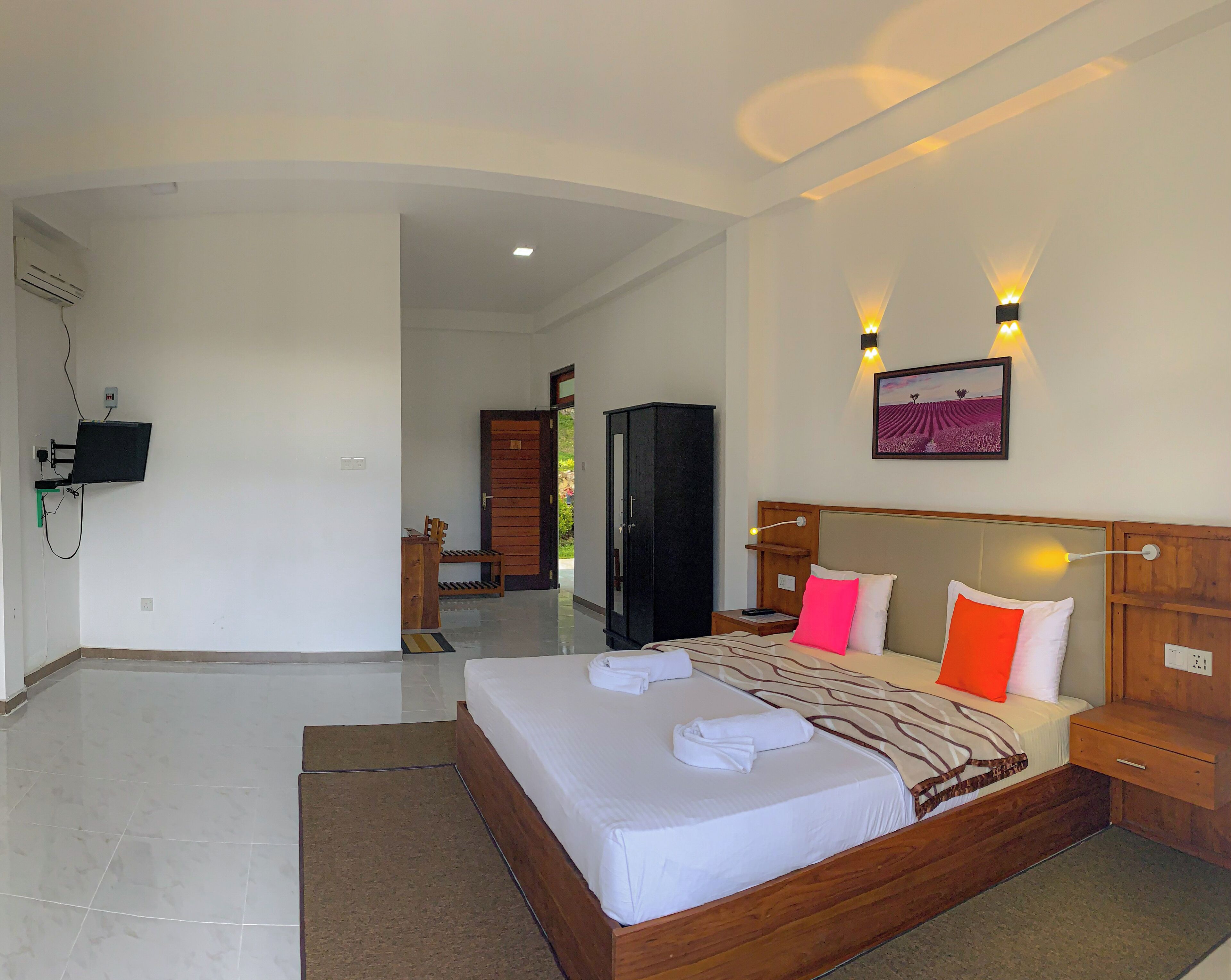 A hotel room with a large bed, a wooden headboard, a flat-screen TV mounted on the wall, and a picture of a field.