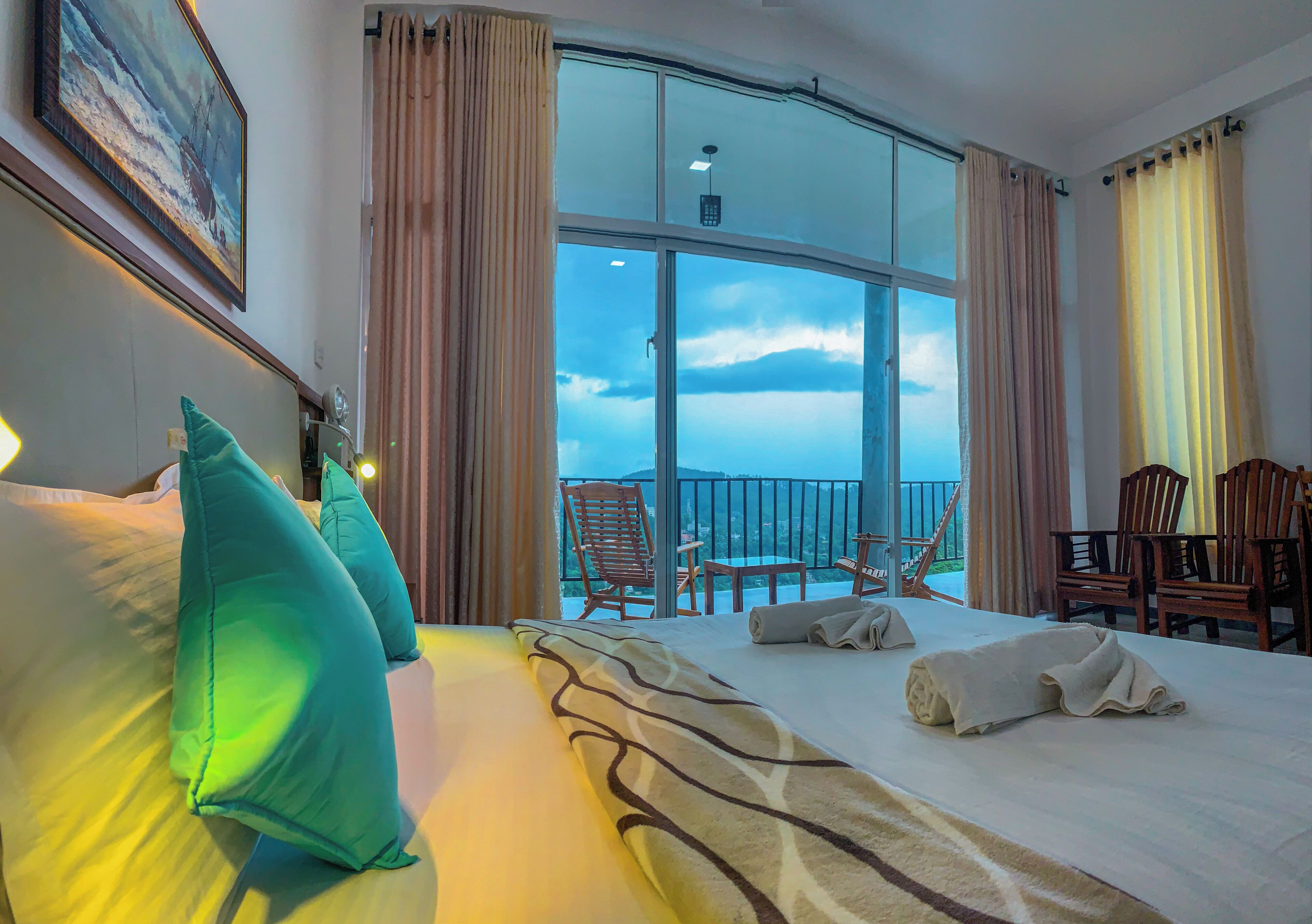 A hotel room with a large bed, a balcony with chairs, and a view of the sky.