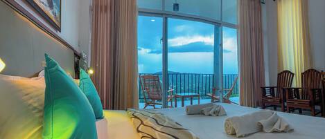 A hotel room with a large bed, a balcony with chairs, and a view of the sky.