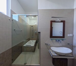 Un baño moderno con ducha envuelta en vidrio, una bañera independiente y un tocador con lavamanos grande.
