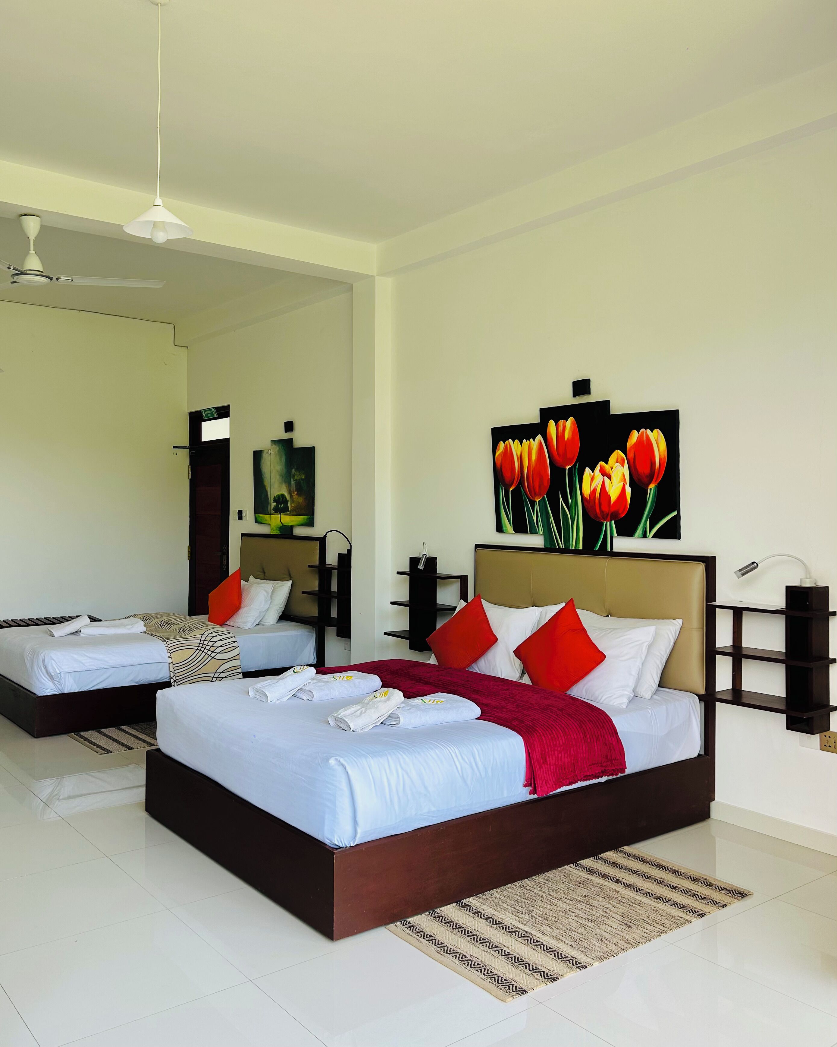 A modern bedroom with a large bed, two smaller beds, a ceiling fan, artwork, and a nightstand.
