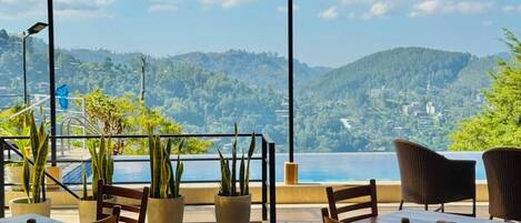A terrace with tables and chairs, potted plants, and a view of a mountainous landscape.