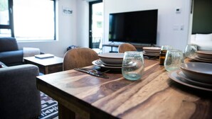 Ein Essbereich mit einem Holztisch, gedeckt für vier Personen, einem Fernseher im Hintergrund und einer Couch im Vordergrund.