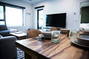 A dining area with a wooden table set for four, a television in the background, and a sofa in the foreground. - Revy Rendezvous | Private Hot Tub & Mountain Views (Revelstoke)