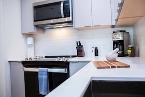 Eine moderne Küche mit Herd, Mikrowelle, Kaffeemaschine und einer Holz-Schneidebrett mit einer Schüssel.