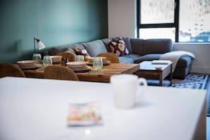 Ein Essbereich mit einem für zwei Personen gedecktem Tisch, einer Couch im Hintergrund und einem Fenster mit Blick.