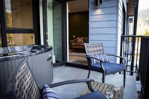 A balcony with a hot tub, a chair with a cushion, and a table with a glass of water. - Revy Rendezvous | Private Hot Tub & Mountain Views (Revelstoke)