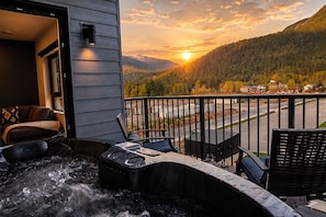 Ein Whirlpool mit Blick auf einen Sonnenuntergang über einem bewaldeten Berg, ein Balkon mit Sitzgelegenheiten und ein Hauseingang.