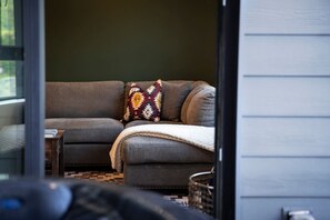 A gray sofa with a patterned pillow and a blanket, a wooden side table, and a view of the outdoors. - Revy Rendezvous | Private Hot Tub & Mountain Views (Revelstoke)
