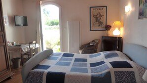 Ein Schlafzimmer mit einem Bett, einem Schreibtisch, einem Stuhl, einem Fernseher und einer Tür, die zu einem Außenbereich führt.