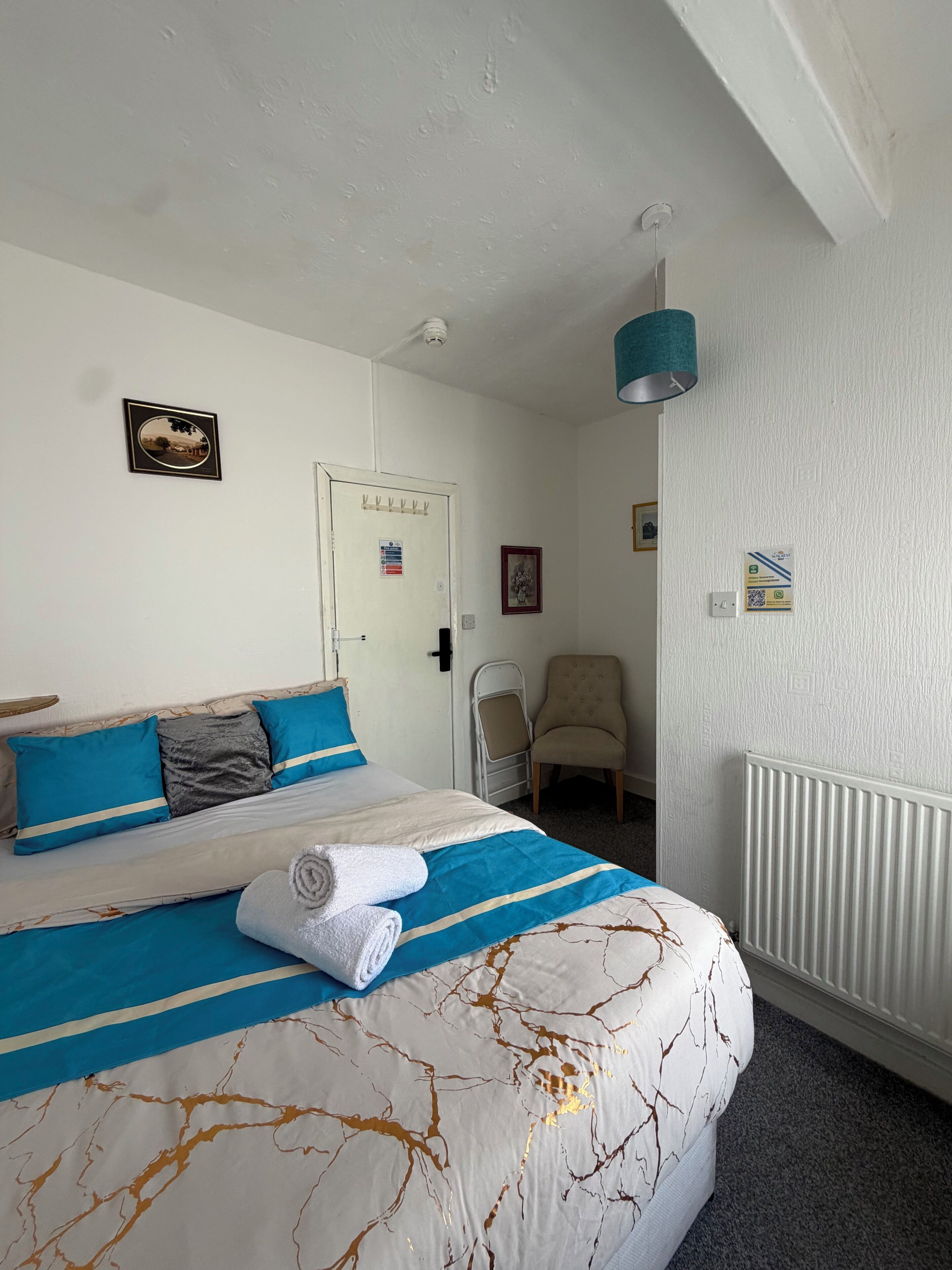 Een hotelkamer met een bed, een stoel, een radiator en een deur met een bordje.