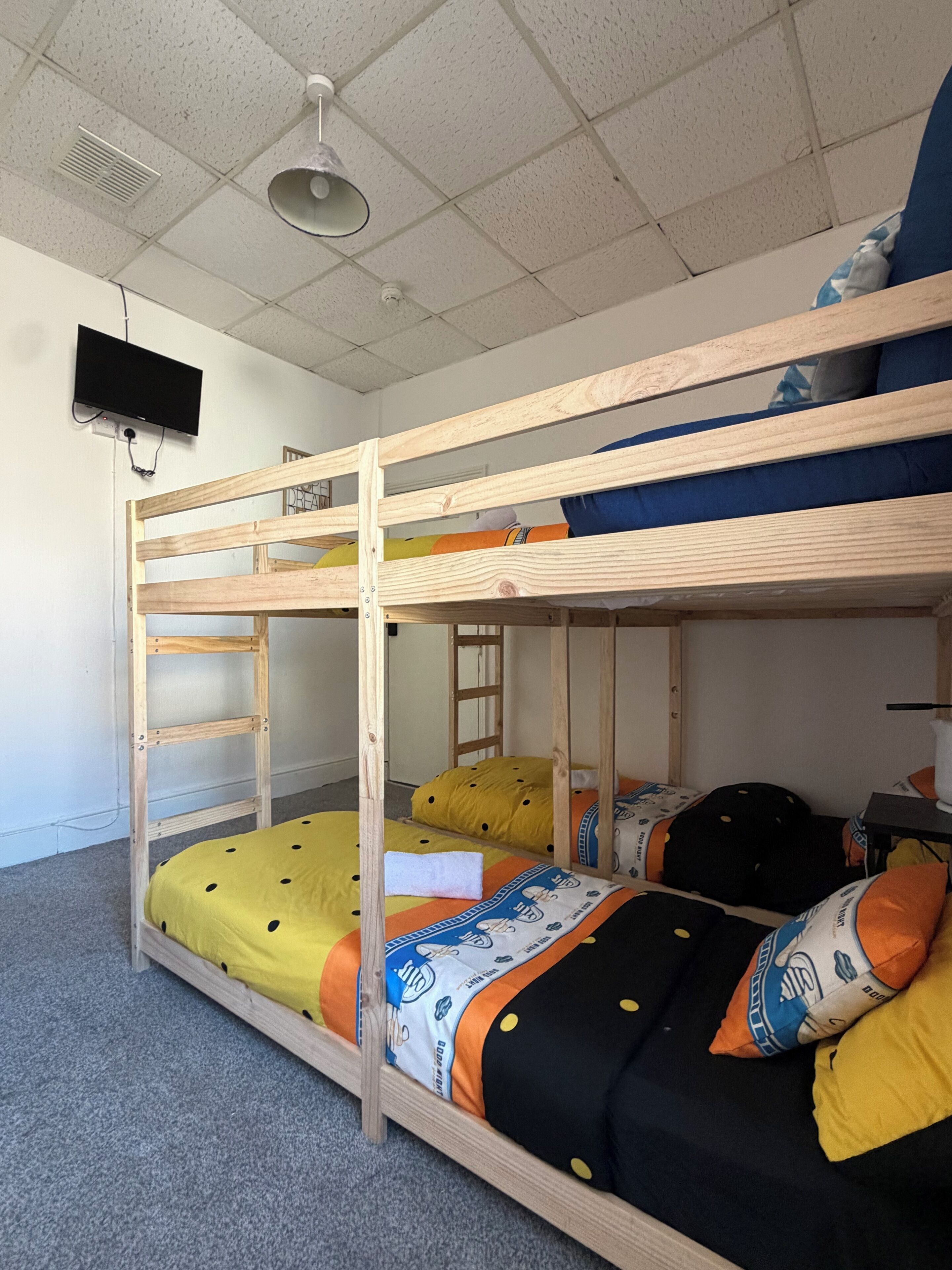 Habitación con literas, televisor montado en la pared, una escalera y un escritorio con silla.