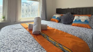 A hotel room with a large bed, a flat-screen TV, a window with curtains, and a wall-mounted artwork. - Suncrest Hotel (Blackpool)