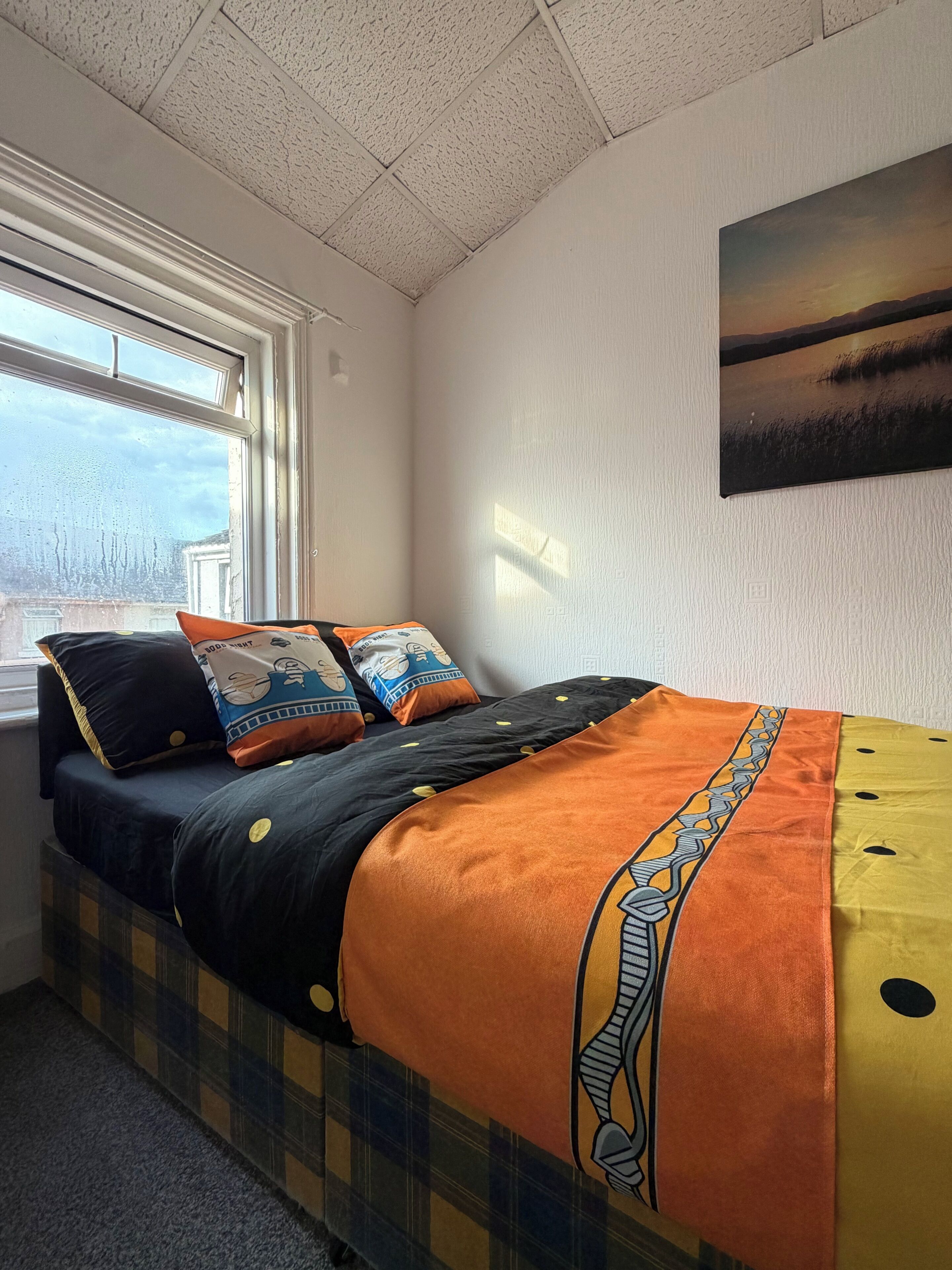 Ein Schlafzimmer mit einem Bett, Kissen, einem Fenster und einem Bild an der Wand.