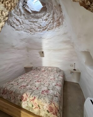 Ett sovrum med en säng, ett litet sängbord, en vägglampa och ett takfönster.
