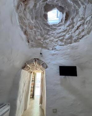Ein Zimmer mit einem Steingewölbe, das auf einen Balkon führt, einer Decke mit einem Oberlicht und einem an der Wand befestigten Flachbildfernseher.